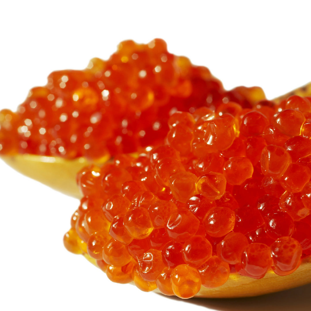 A glass jar of fresh salmon roe stored on ice in a refrigerator alongside other premium caviar products