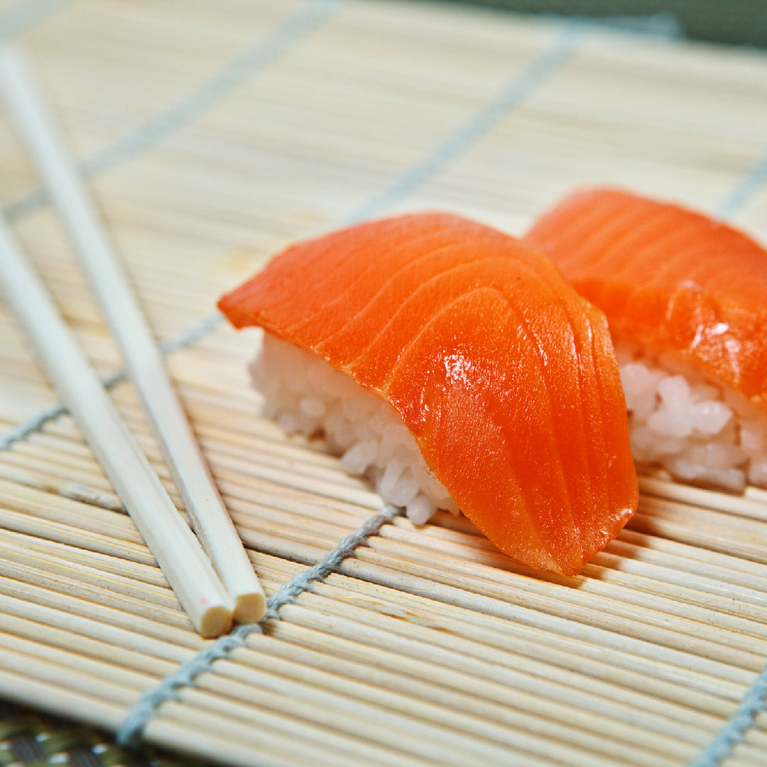 Salmon nigiri on a bamboo mat beside chopsticks.