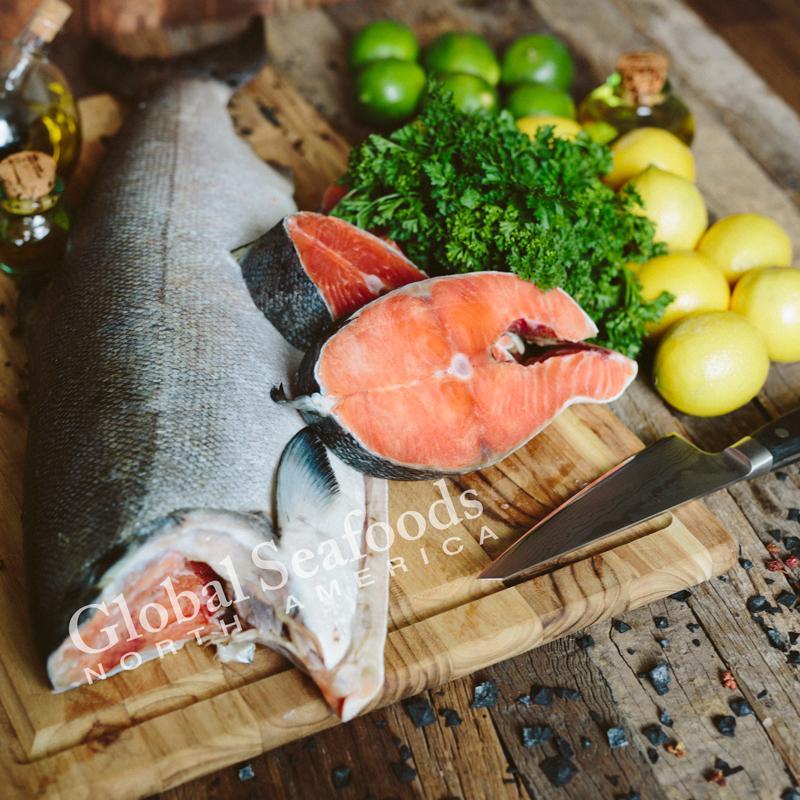 Whole sockeye salmon grilling over open flame on a charcoal grill with lemon and dill