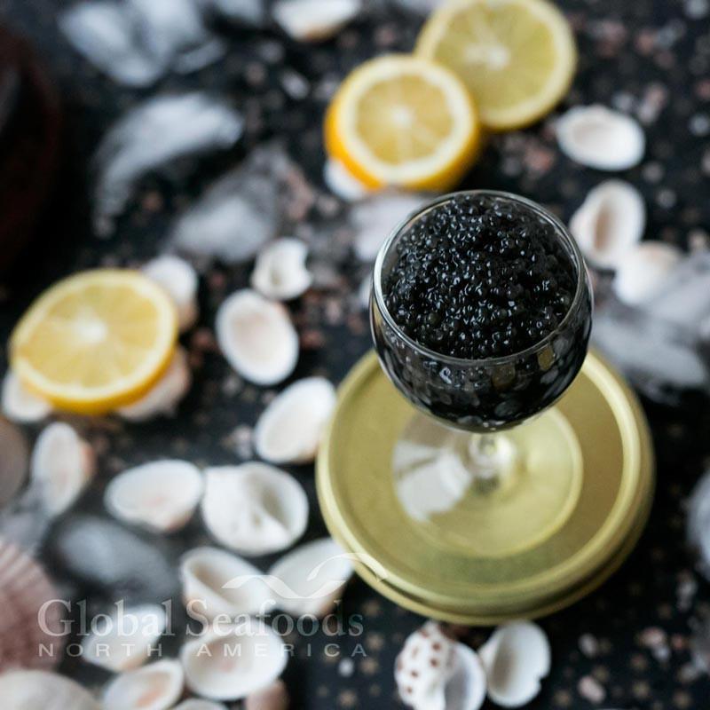 Side-by-side comparison of real sturgeon black caviar (glossy, uniform eggs) and fake imitation caviar (dull, irregular) on a white plate