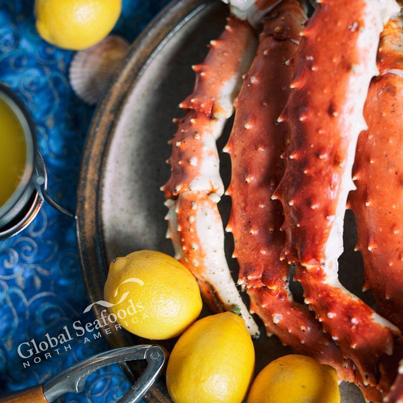 Grilled Alaskan king crab legs on a barbecue grill with lemon wedges and garlic butter dipping sauce