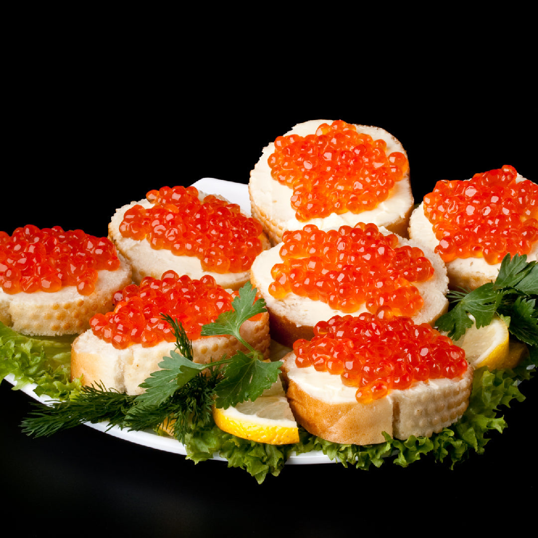 Vibrant orange Atlantic salmon roe pearls served in a small glass bowl on crushed ice, garnished with fresh dill alongside blinis and sour cream