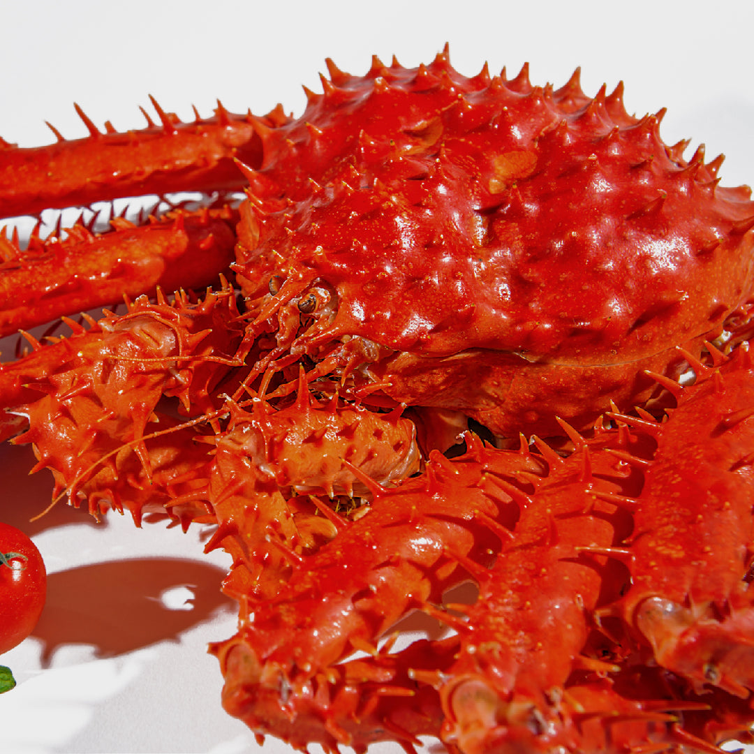 King crab legs displayed on ice at a seafood market with price tags showing global cost comparison