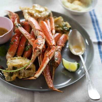 Snow crab legs grilling on an outdoor barbecue with charred marks, garnished with lime wedges and fresh cilantro