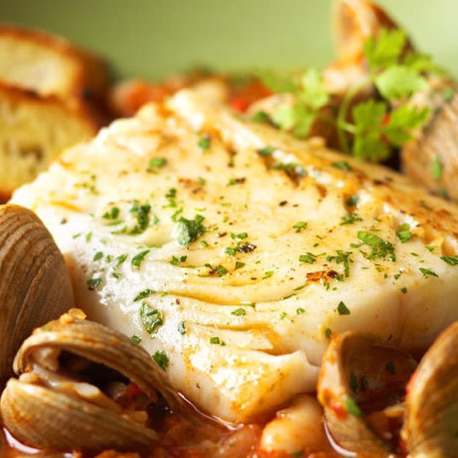 Seared black cod fillet served over sofrito broth with clams, white beans, and chorizo, garnished with fresh parsley