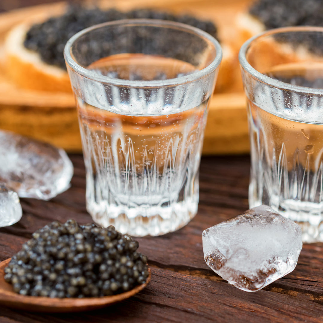 Beluga caviar served in its tin on crushed ice alongside a flute of Champagne, with mother-of-pearl spoon and blini on a marble surface
