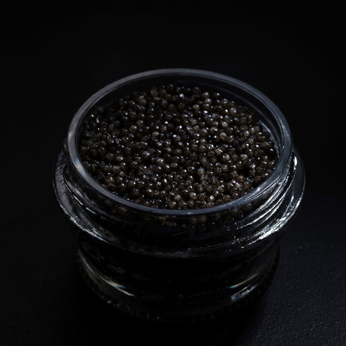 Beluga caviar pearls served on a mother-of-pearl spoon with blinis and champagne in the background