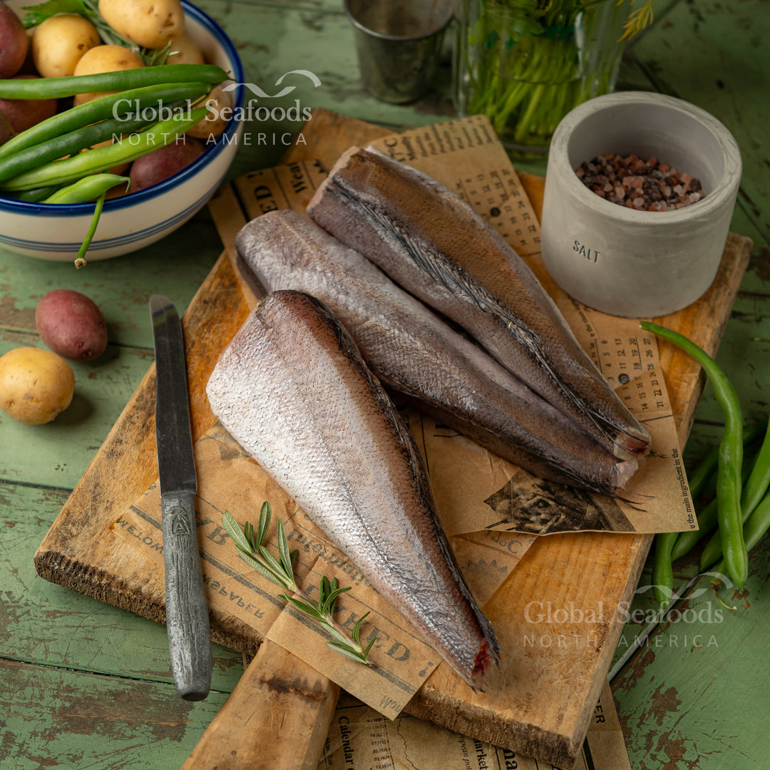 Hake fish fillet being pan-fried in garlic butter in a skillet