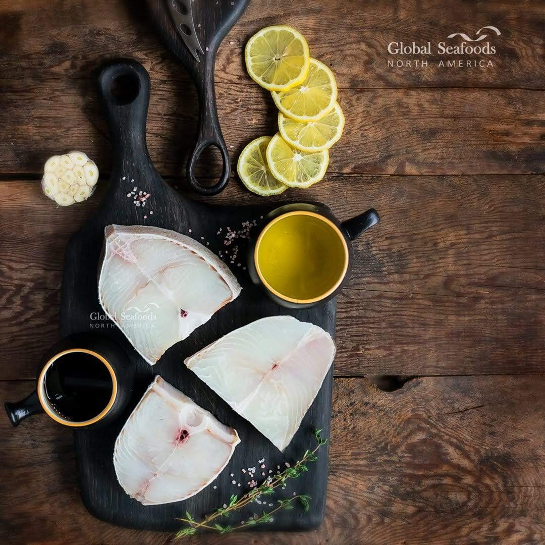 Array of fresh ingredients for poached halibut recipe, including mirin, shallots, fresh herbs, and halibut fillets, arranged neatly on a kitchen countertop