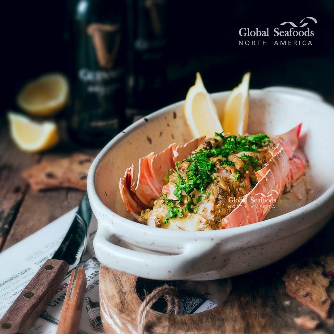 Close-up image of a perfectly cooked lobster with a bright red shell and juicy, white meat, set against a backdrop of fresh herbs and lemon, illustrating the delicious outcome of proper lobster cooking techniques