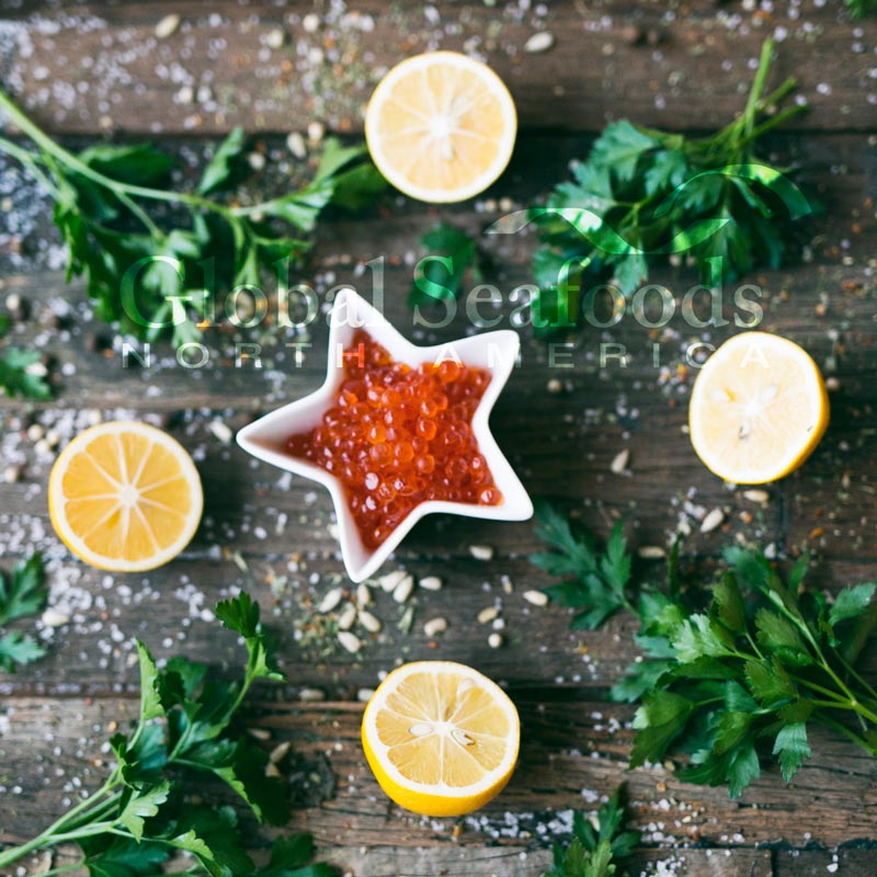 Hands rinsing bright orange salmon roe in a fine mesh strainer over a bowl of cold water