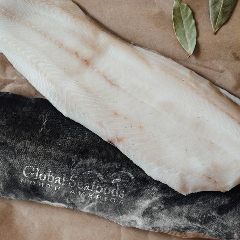 A beautifully baked sablefish fillet on a white plate, garnished with lemon slices and fresh herbs, showcasing the dish's golden-brown crust and moist, flaky texture, ready to be enjoyed