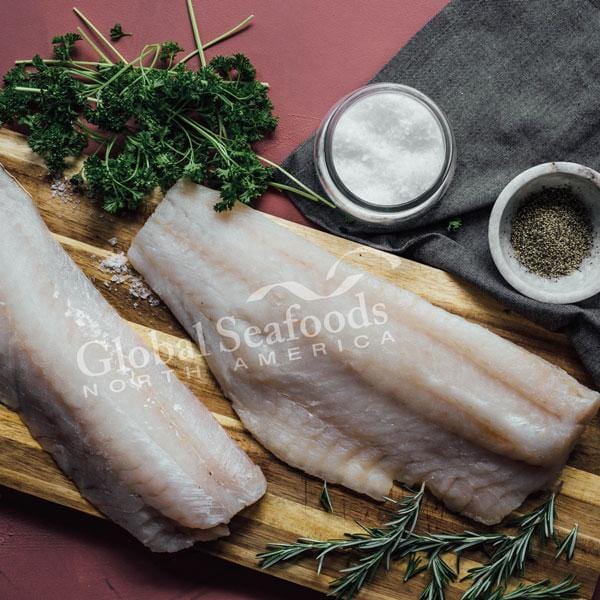 Fresh Pacific cod fillet on a plate with lemon slices and herbs, showcasing its firm white flesh and clean appearance