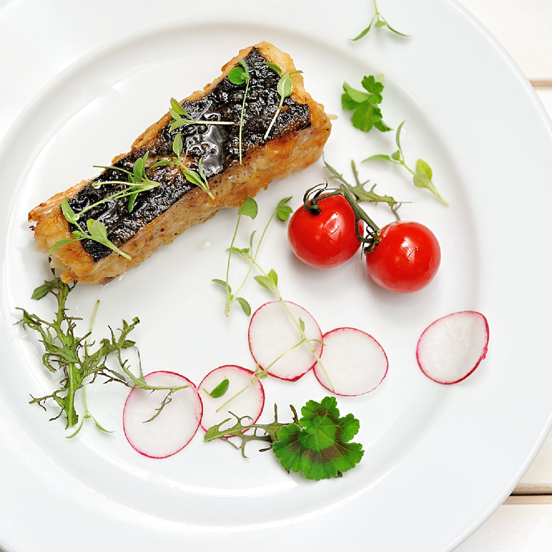 Cooked skin-on fish with cherry tomatoes, sliced radishes and herbs.