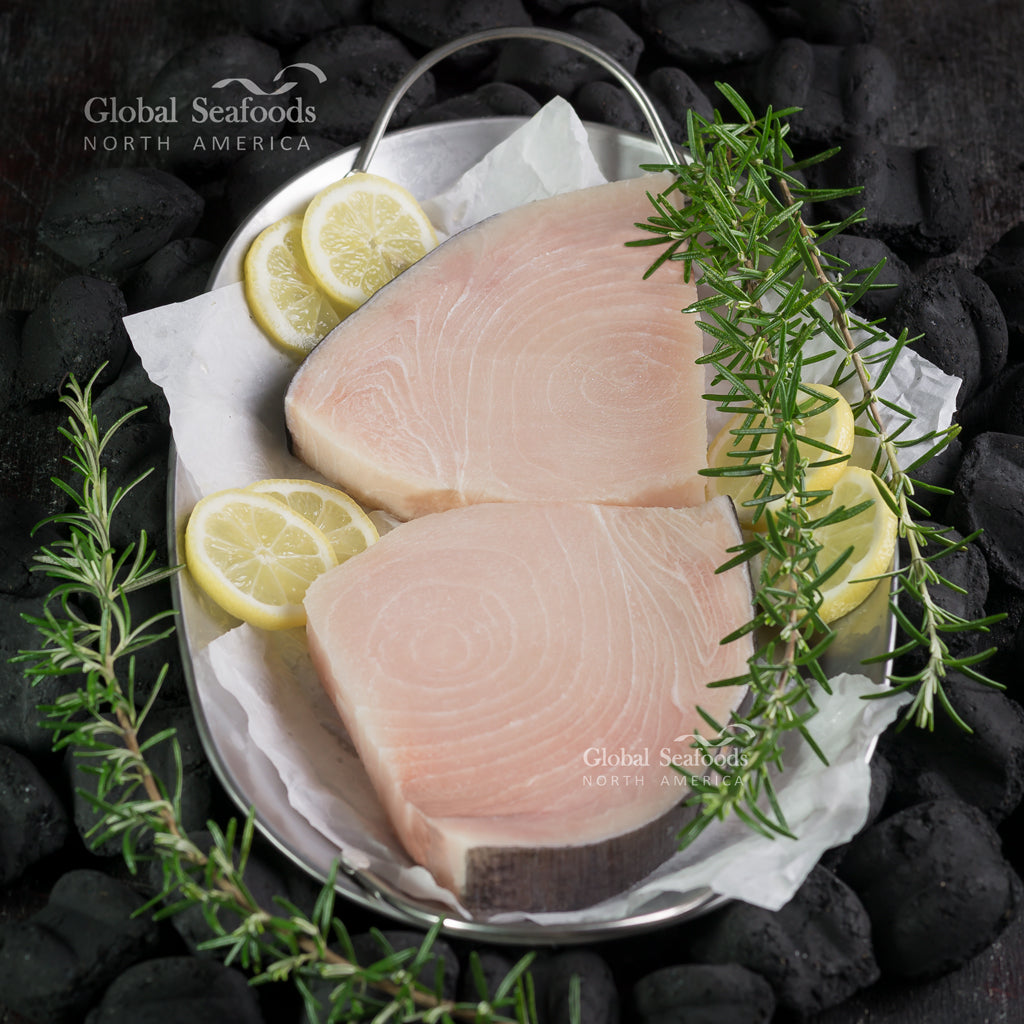 Sizzling swordfish steak searing on a hot Himalayan salt rock with lemon wedges and fresh herbs