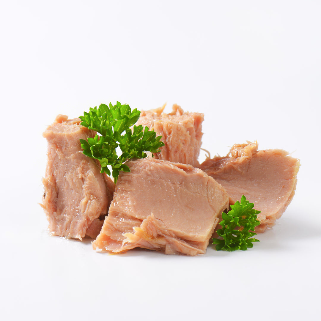 Creamy albacore tuna dip in a white bowl garnished with paprika and fresh dill, surrounded by crackers, pita chips, celery sticks, and cucumber slices