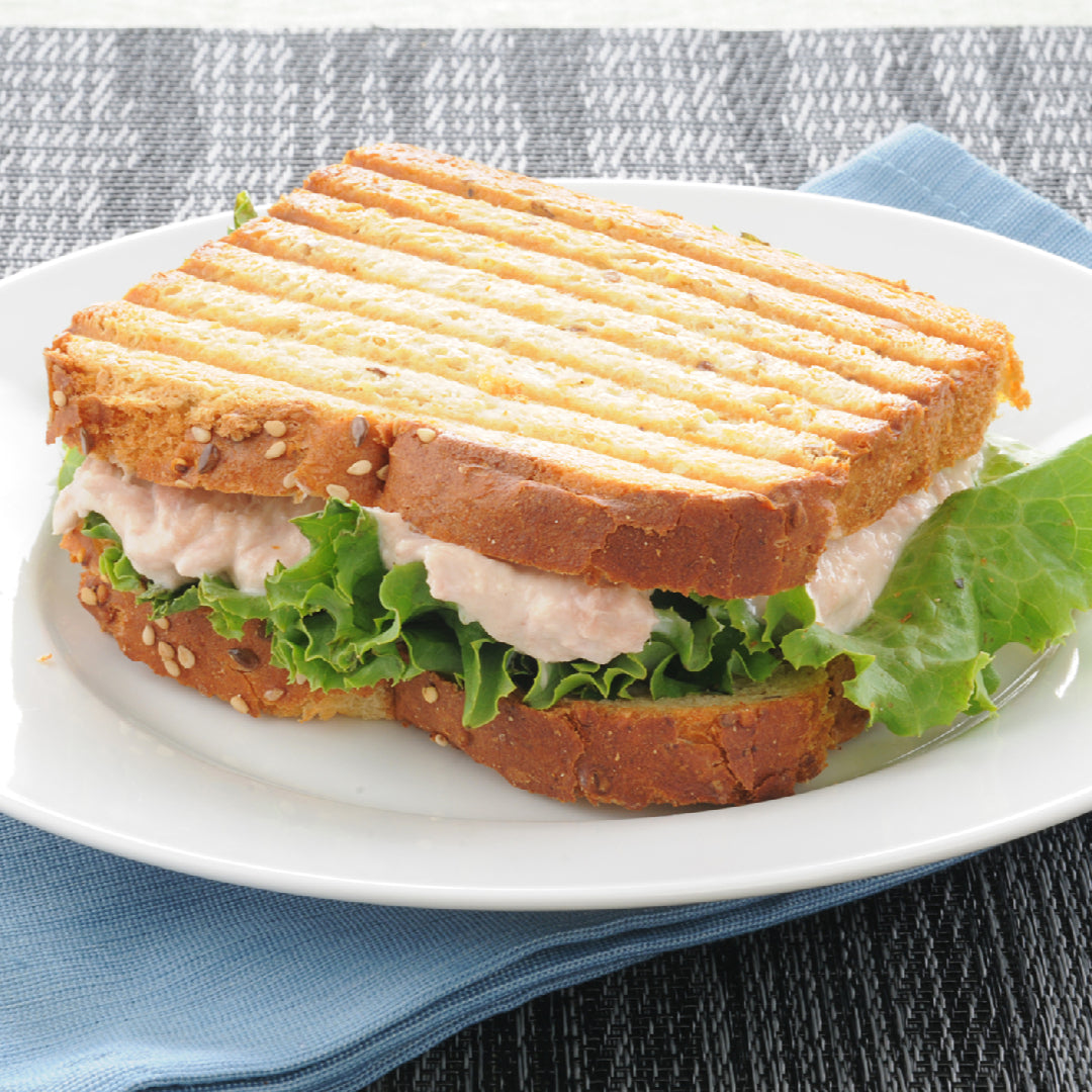 Grilled albacore tuna steak sliced over mixed greens with cherry tomatoes, avocado, red onion, cucumber, and lemon Dijon dressing in a white bowl