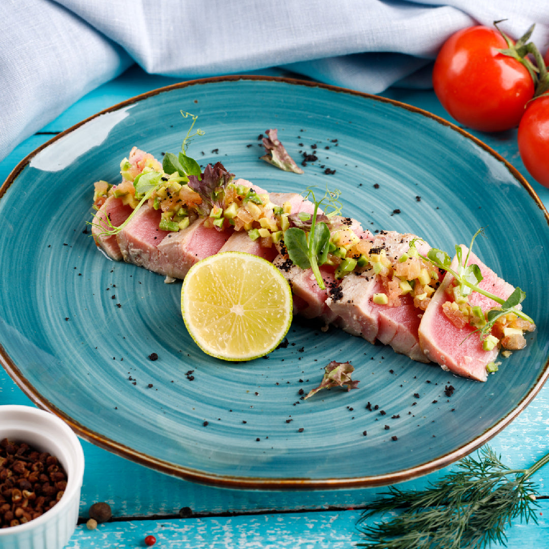 Perfectly grilled albacore tuna steak with grill marks, lemon, and fresh herbs