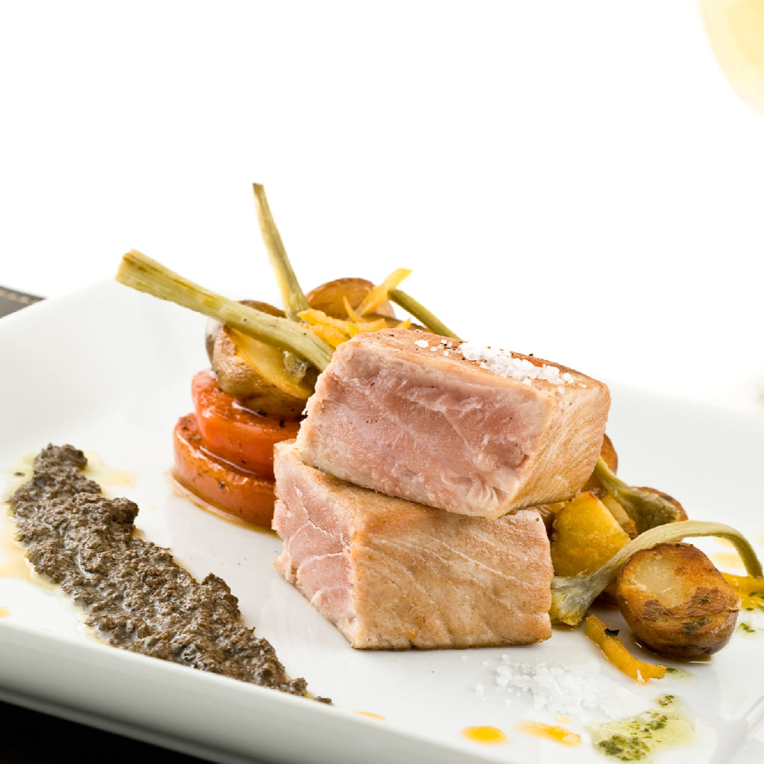 Oven-baked albacore tuna fillet garnished with fresh parsley and lemon slices on a white plate