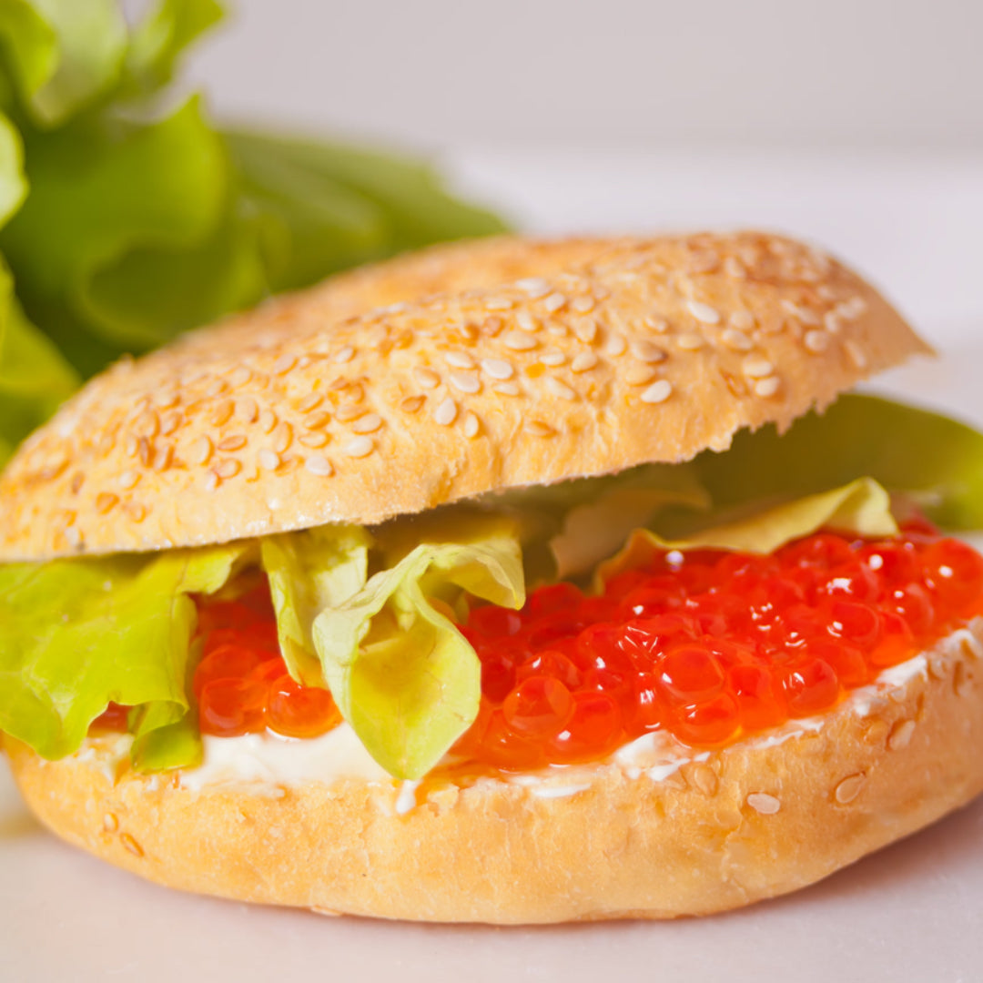 Creamy red caviar spread on a toasted bagel half, garnished with fresh dill and lemon zest, served alongside smoked salmon and cucumber slices for a gourmet brunch