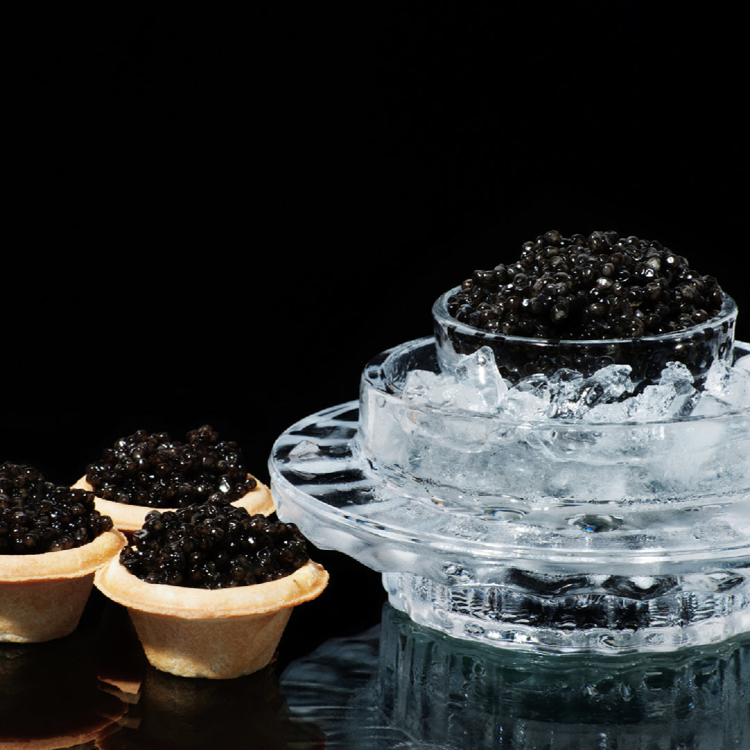 Elegant caviar tasting party setup with multiple caviar varieties on crushed ice, mother-of-pearl spoons, blinis, crème fraîche, and Champagne glasses on a decorated table