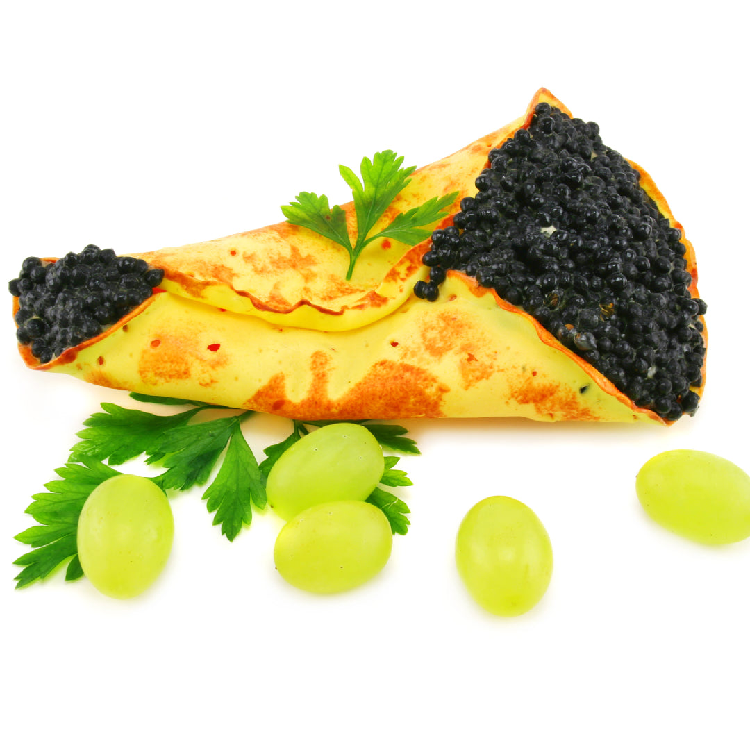 Kaluga caviar in a glass serving dish over ice: large, dark gray pearls with a glossy surface, served with a mother-of-pearl spoon and blinis alongside
