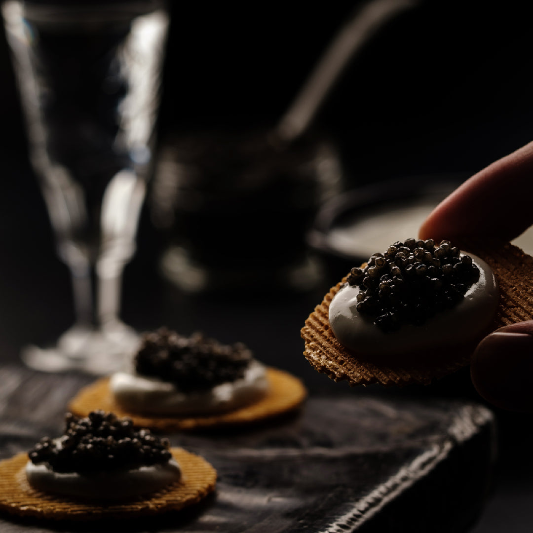 Close-up of glossy Kaluga caviar pearls served on a mother-of-pearl spoon with blinis and crème fraîche on a dark elegant surface
