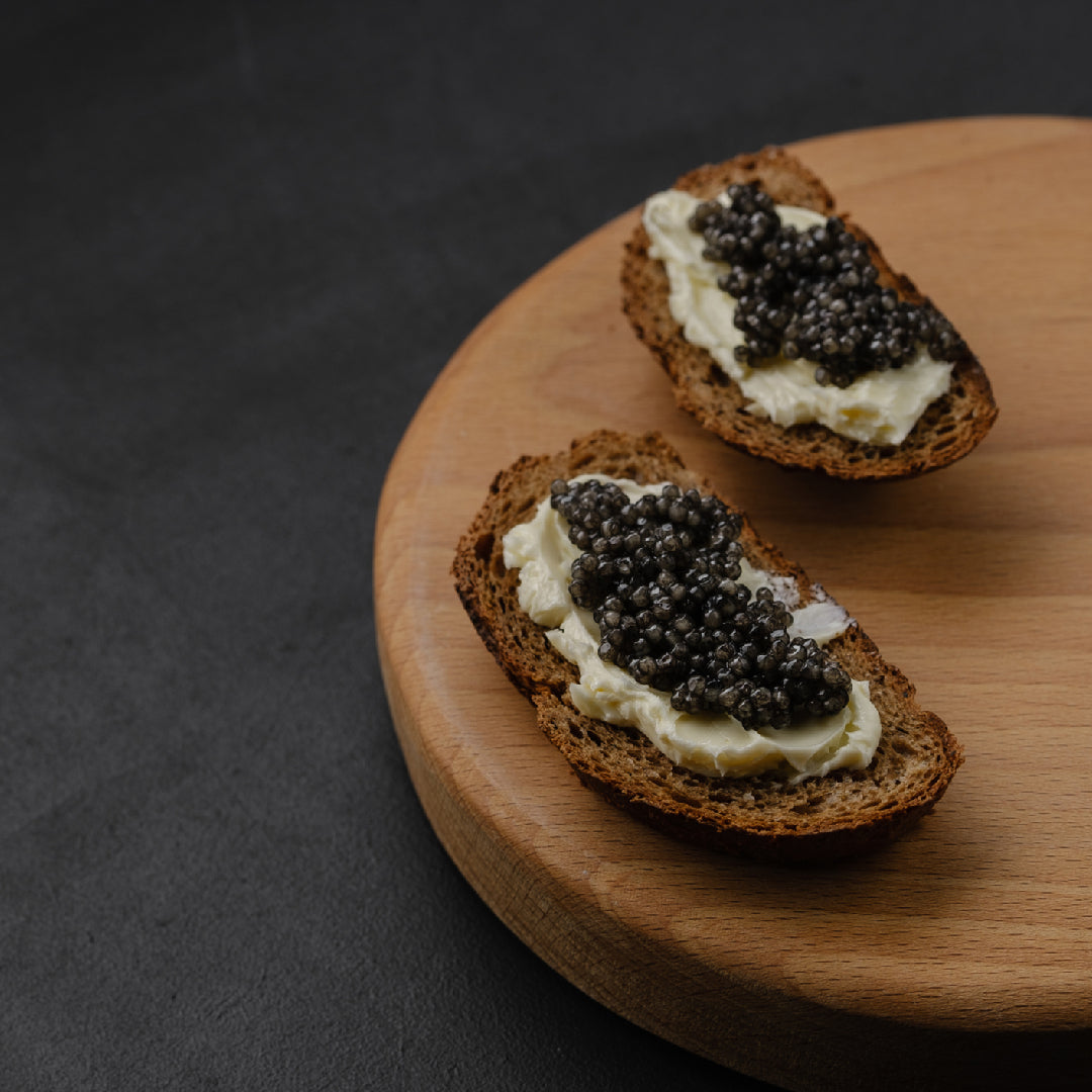 Premium Kaluga caviar tin open on a marble surface with a mother-of-pearl spoon, blinis, and a glass of champagne