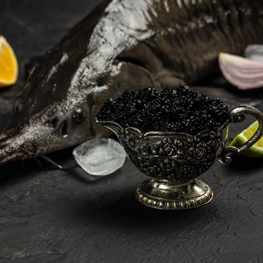 Kaluga caviar pearls in an open tin displayed on crushed ice next to a mother-of-pearl spoon and a glass of champagne on a dark luxury surface