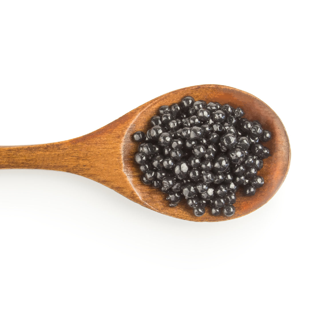 Kaluga caviar and Beluga caviar side by side in mother-of-pearl spoons on a dark slate surface with blinis and champagne