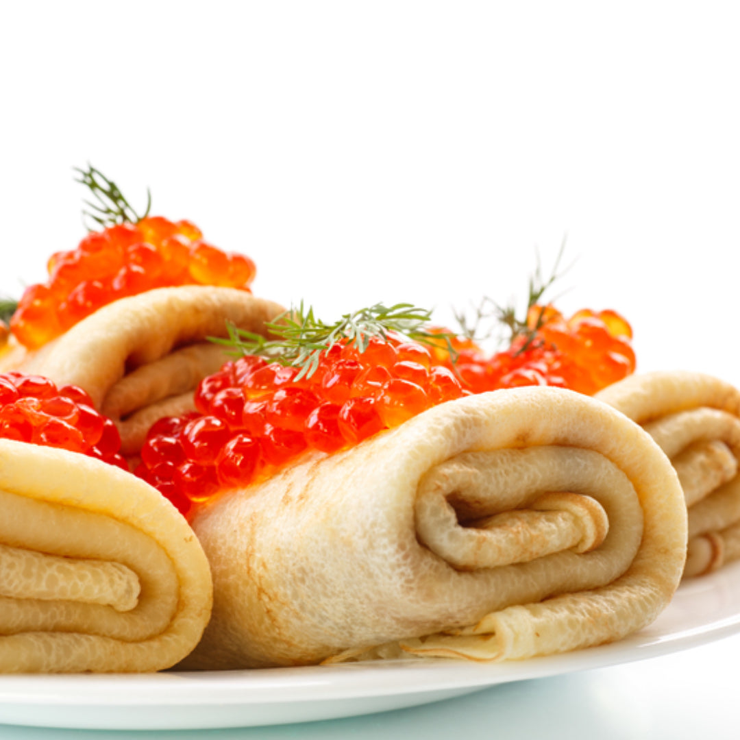 Elegant serving of blinis topped with crème fraîche and glistening orange salmon caviar, garnished with fresh dill on a white plate