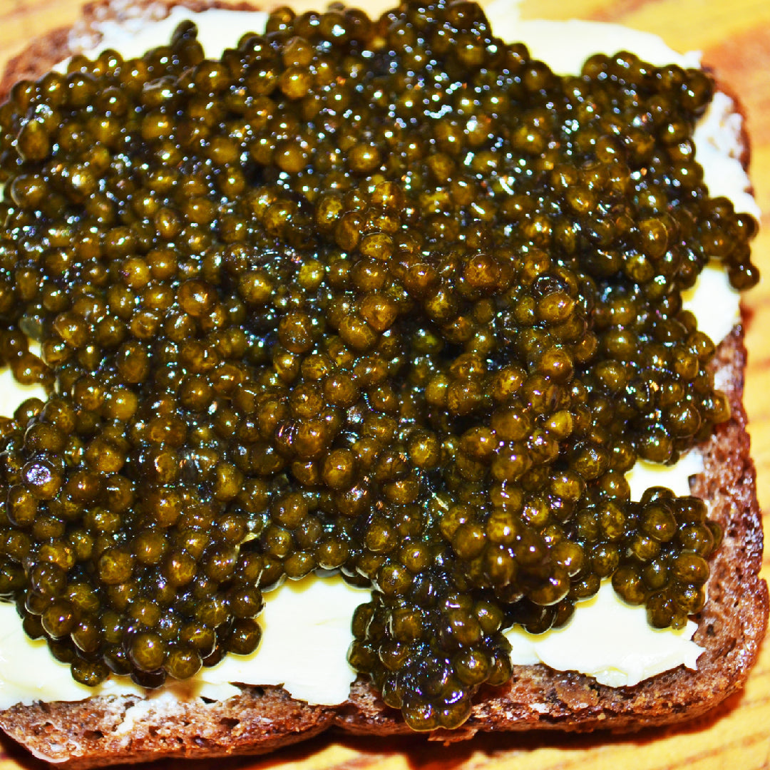 Beluga caviar served on a mother-of-pearl dish with blinis and garnishes on a bed of crushed ice
