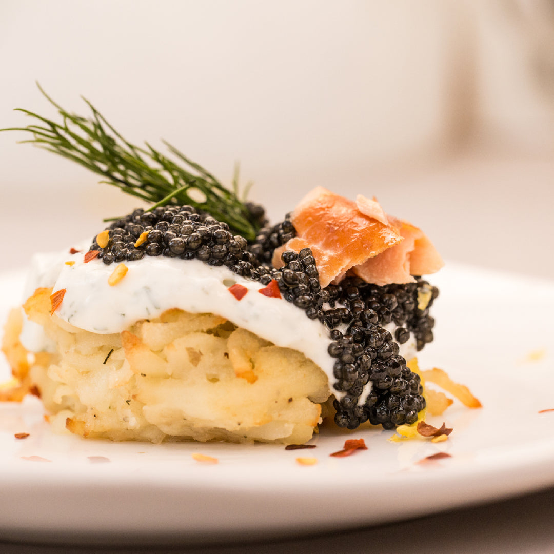 Premium Kaluga caviar pearls in an open tin on crushed ice with a mother-of-pearl spoon, blinis, and champagne on a luxury dining table