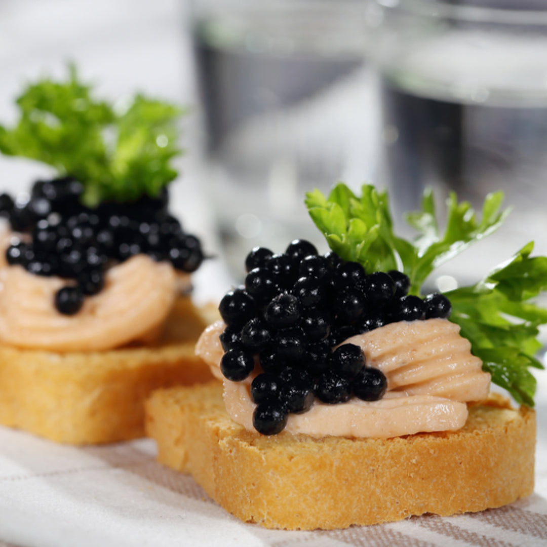 Caviar on toast served on a white marble board – crispy sourdough topped with crème fraîche, black sturgeon caviar, fresh chives, and a lemon wedge