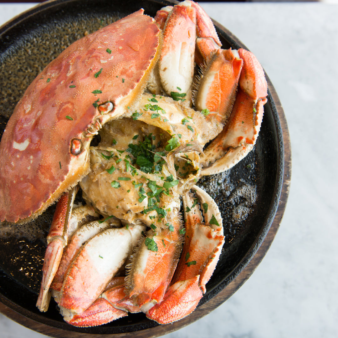 A platter of garlic butter crab claws garnished with fresh parsley and lemon wedges, styled for an Instagram-worthy seafood presentation