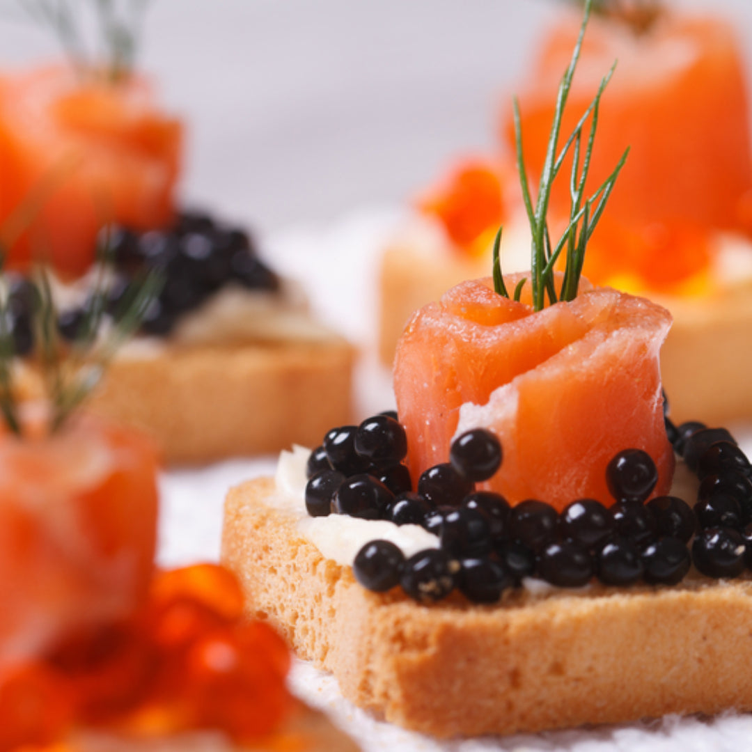 Elegant caviar canapés on toasted baguette slices topped with cream cheese and black sturgeon caviar, garnished with fresh dill on a marble serving board