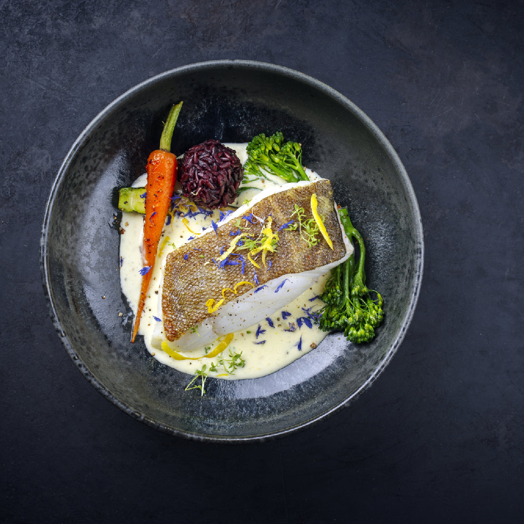 Pan-seared Sablefish fillet over roasted sweet potatoes and Brussels sprouts on a white plate with fresh herbs