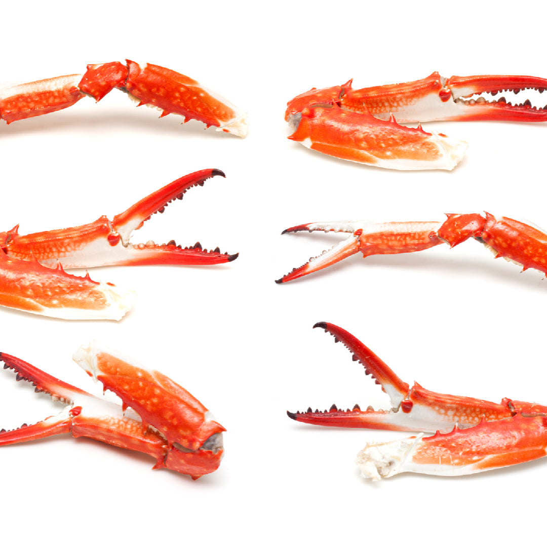A platter of crab claws served with small bowls of lemon garlic butter, Sriracha mayo, and herb aioli dipping sauces on a wooden board