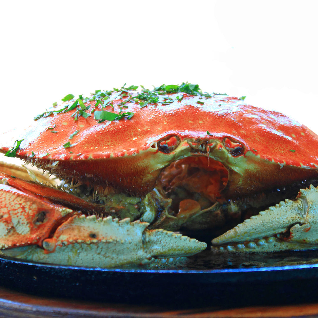Steamed Dungeness crab clusters on a platter with melted garlic butter, lemon wedges, and fresh parsley