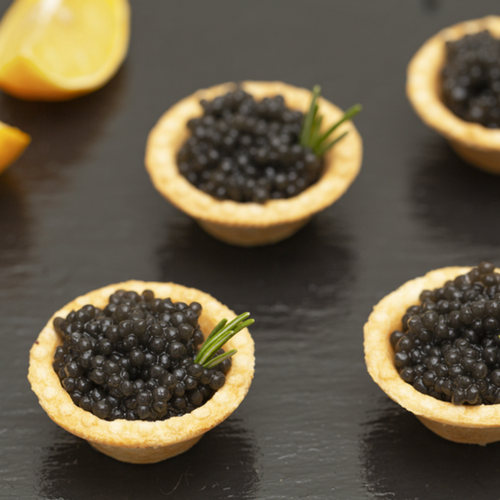 Elegant caviar appetizers served on blinis with crème fraîche and fresh dill on a marble board