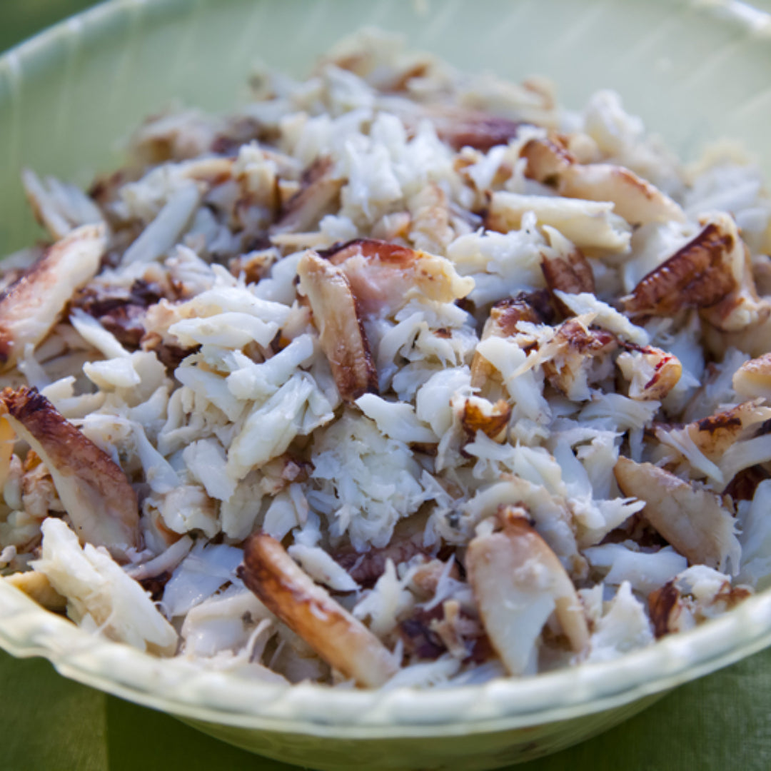 Fresh raw crab meat in a bowl with lemon, chives, and seasoning on a marble surface