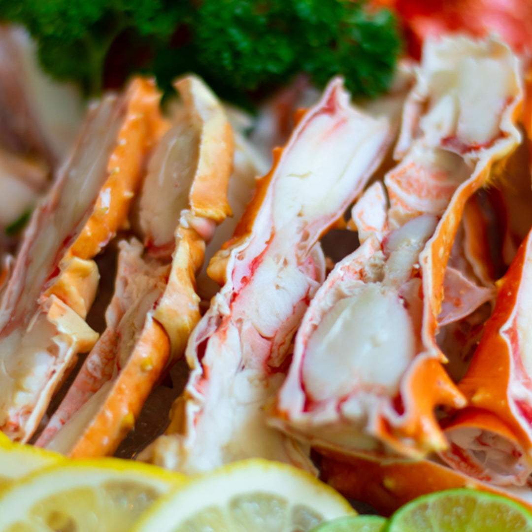 Steamed Norwegian red king crab legs split open and served with garlic butter and lemon on a wooden board