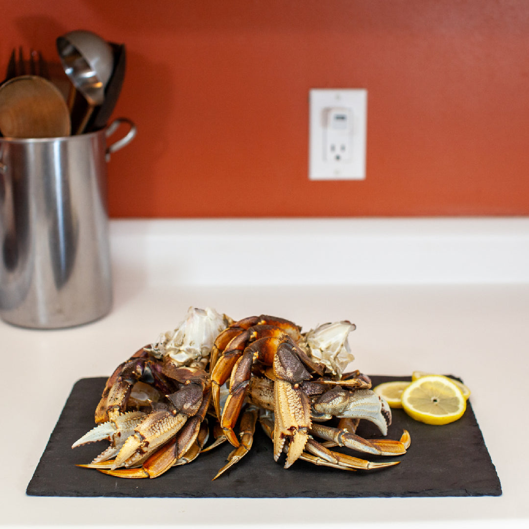 Perfectly cooked Dungeness crab leg clusters on a white platter with melted butter, lemon wedges, and fresh herbs