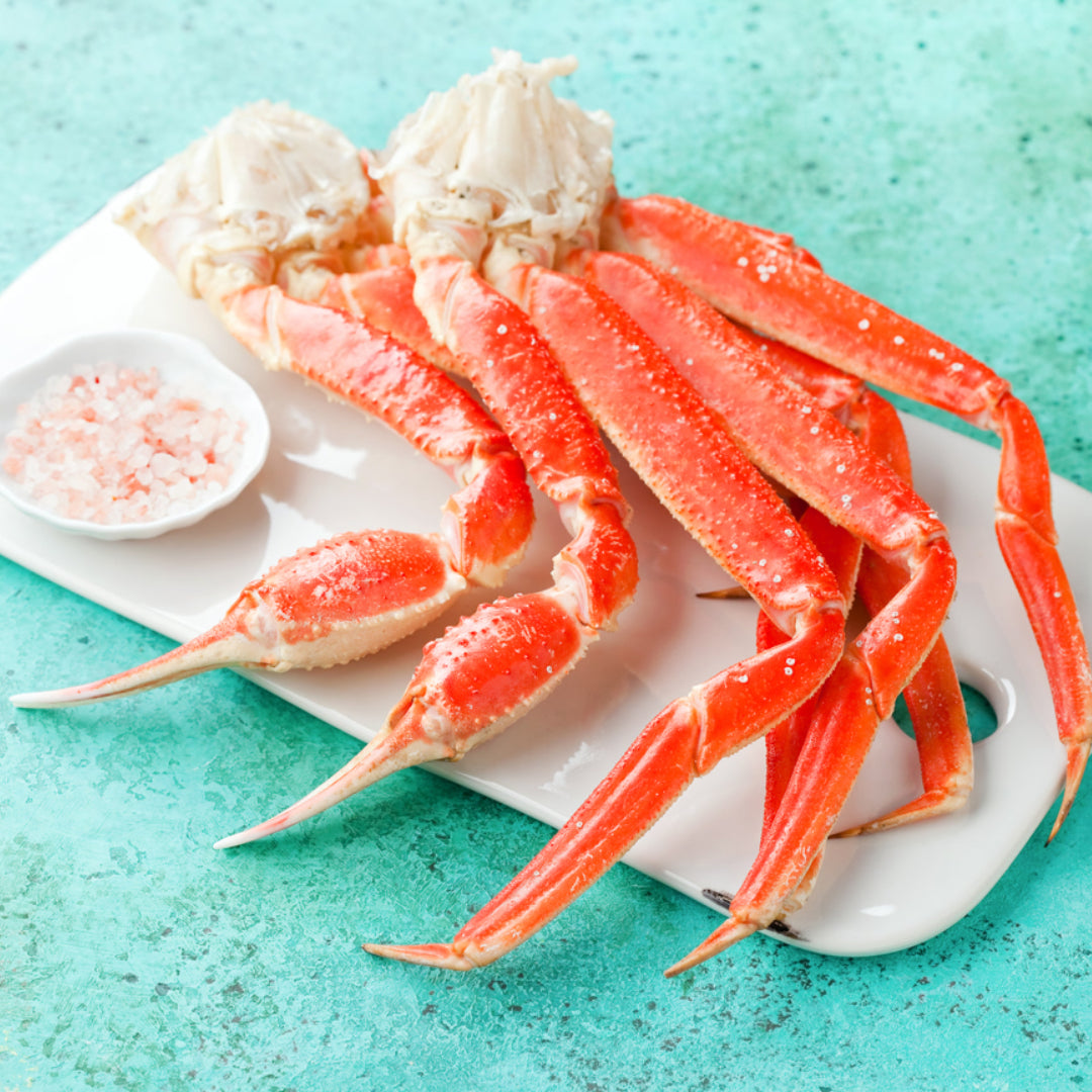 Steamed snow crab leg clusters on a platter with melted garlic butter, lemon wedges, and fresh parsley