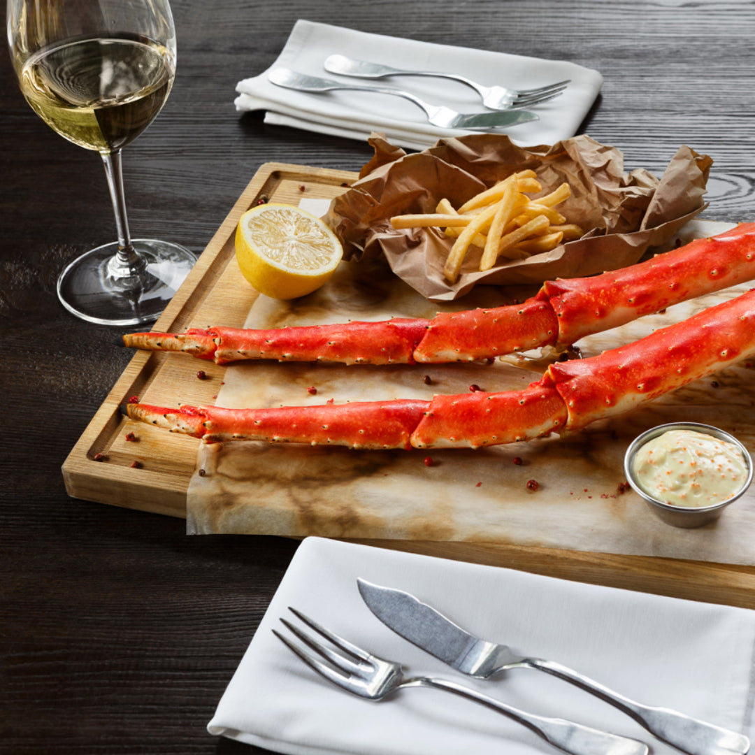 A wine glass and a plate of crab with lemon wedges and parsley on a wooden table