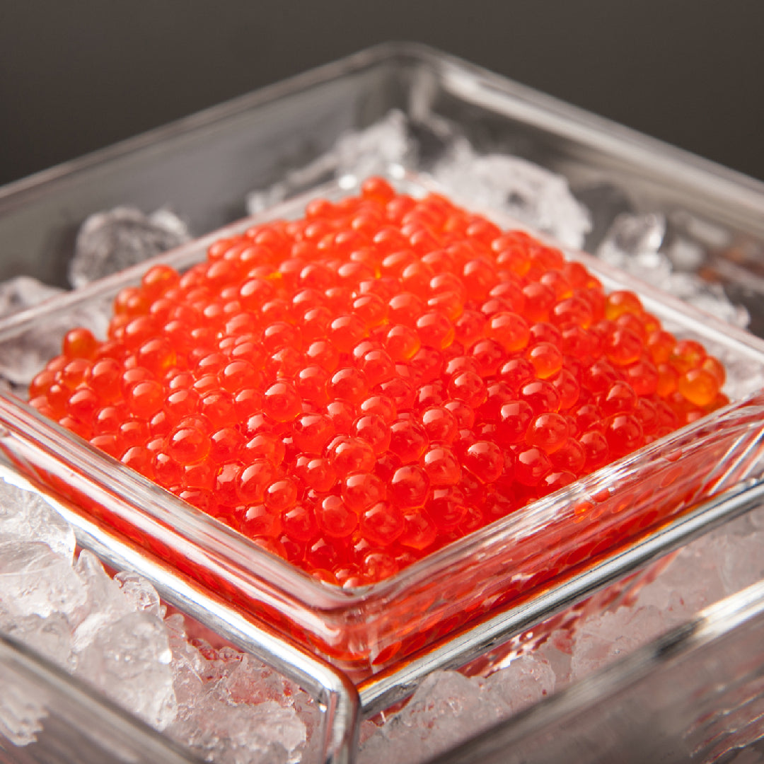 Glistening orange-red ikura salmon roe in a ceramic bowl with a mother-of-pearl spoon on a dark wooden surface