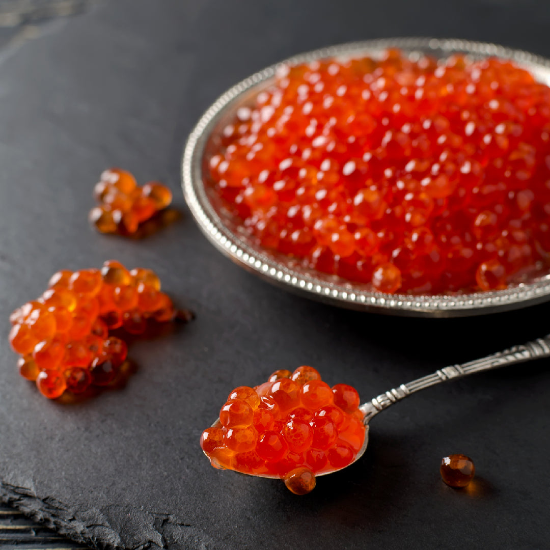 The history of IKURA caviar – glistening red-orange salmon roe pearls in a traditional serving bowl, tracing the journey of this luxury delicacy from 16th-century Russian royalty through Japanese sushi culture to modern global fine dining