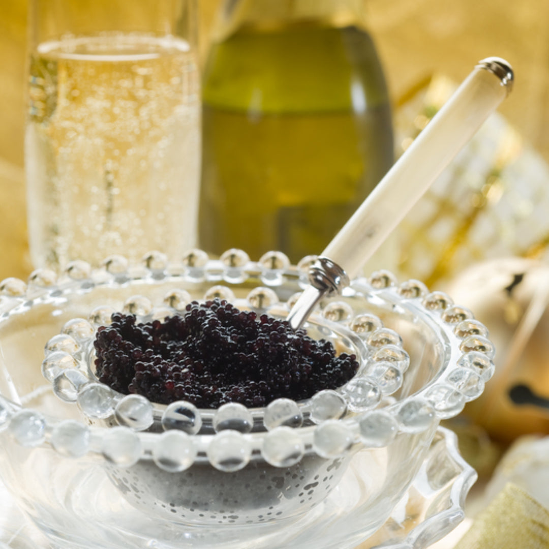 Dark glossy Louisiana paddlefish caviar served on a mother-of-pearl spoon with blinis and crème fraîche