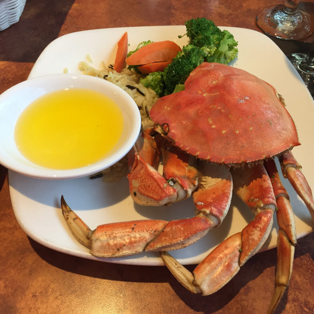 Whole Dungeness crab being cleaned on a cutting board — top shell removed, gills visible before removal, showing the step-by-step process of preparing Dungeness crab for cracking and eating