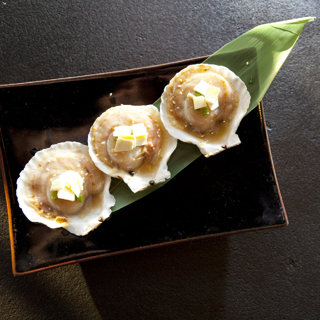 Fresh diver scallops being cleaned on a cutting board with a paring knife, paper towels, and a bowl of cold water